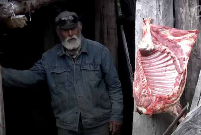 old man in a makeshift building with side of meat hanging outside
